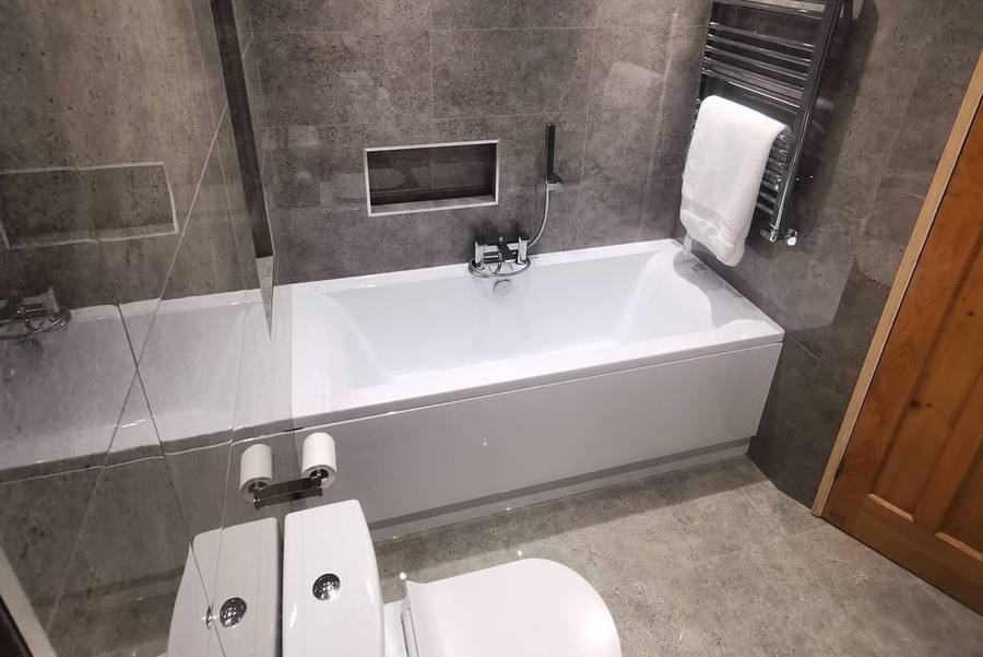 A finished bathroom with a white bath, chrome towel rail and tiled recess
