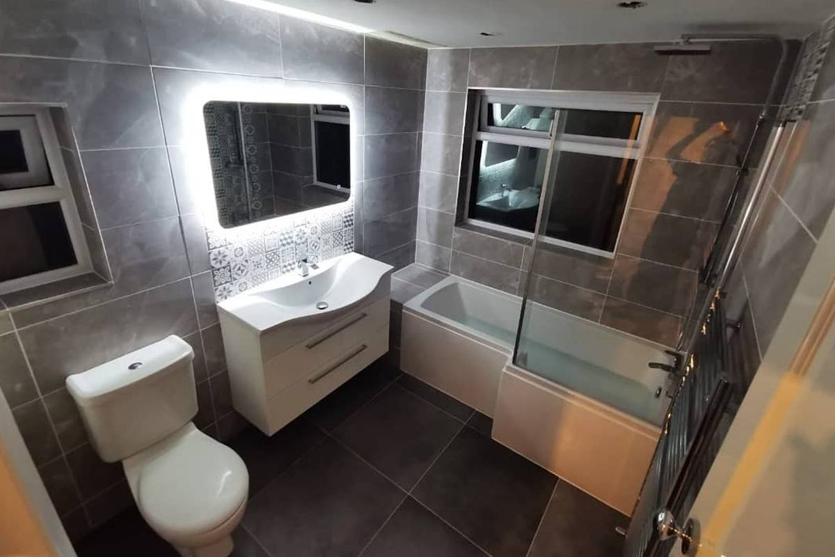 A finished grey tiled bathroom with a backlit mirror and a vanity unit
